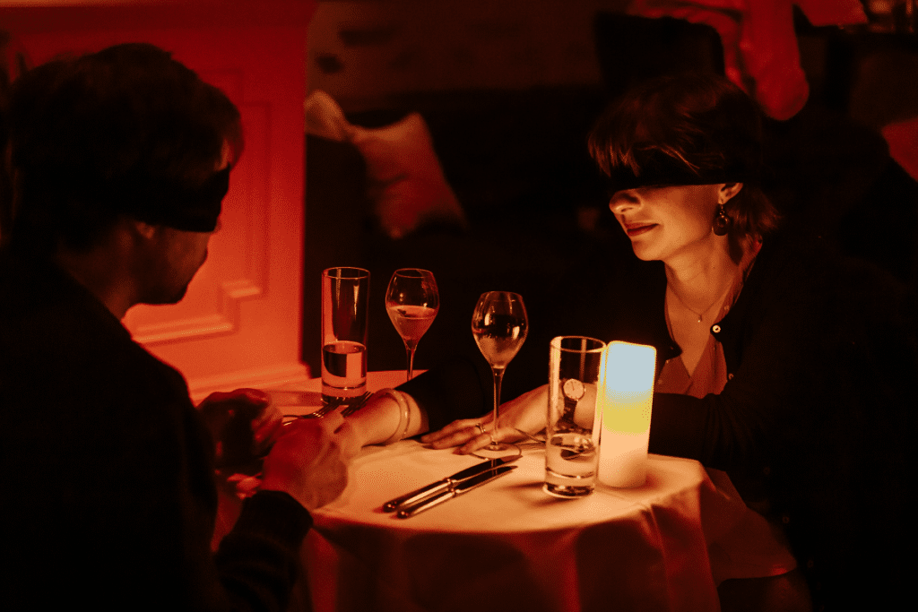 A blindfolded couple enjoying a meal and a glass of wine at Dining in the Dark