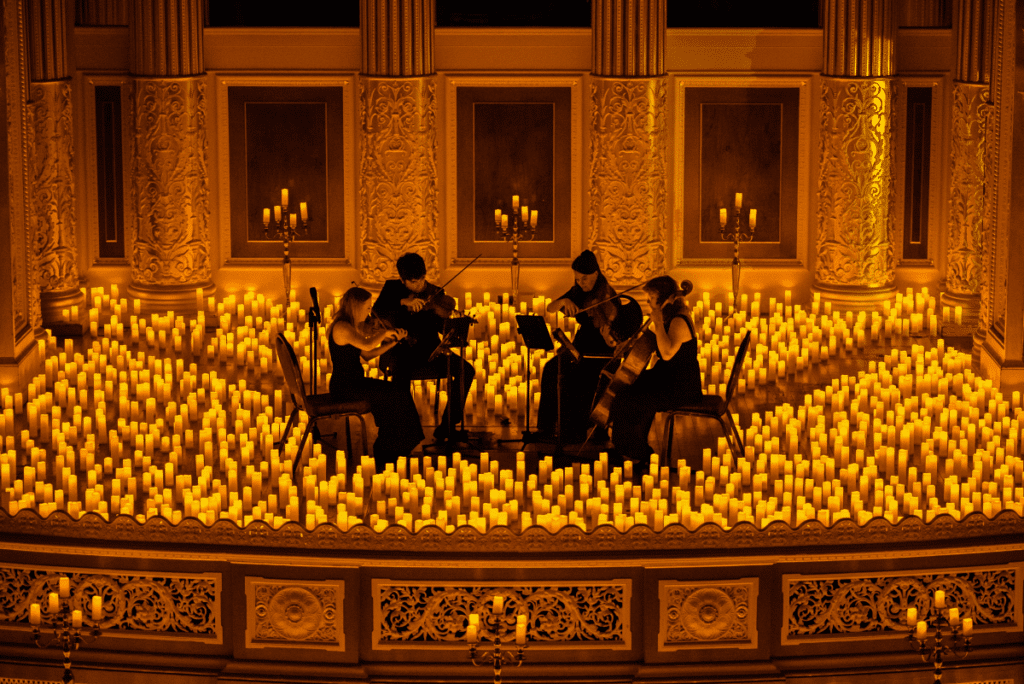 A string quartet performing on a stage surrounded by a sea of candles with an ornate background reasons why to attend candlelight concert