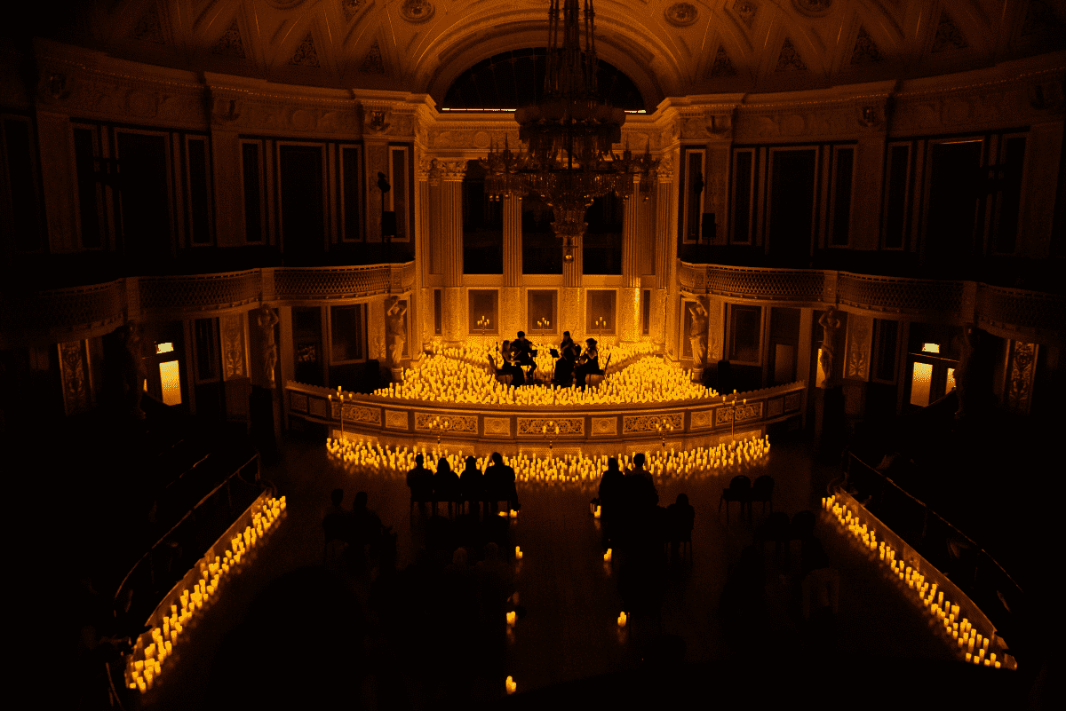 A string quartet performing on a stage glowing in candlelight and the audience in darkness.
