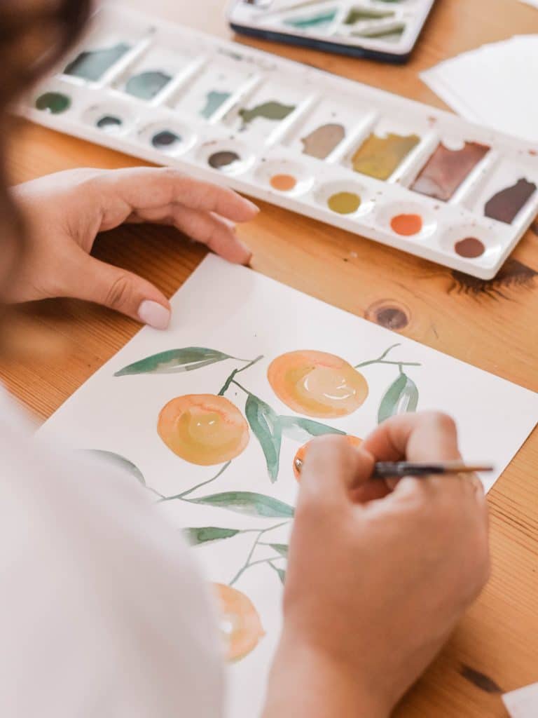 A person paints an orange tree in watercolour.