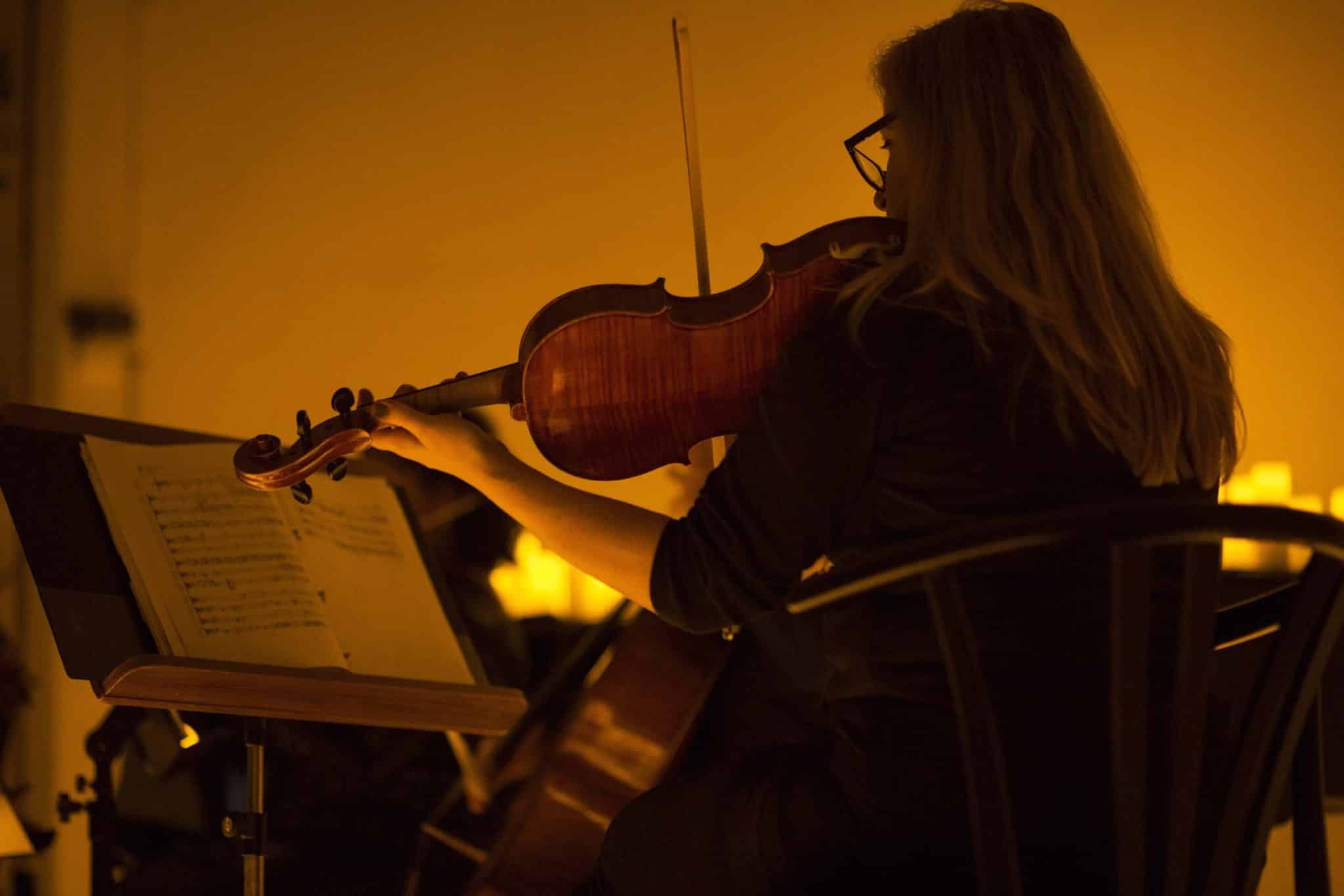 A woman playing violin, lit by candlelight at a Candlelight Concert.