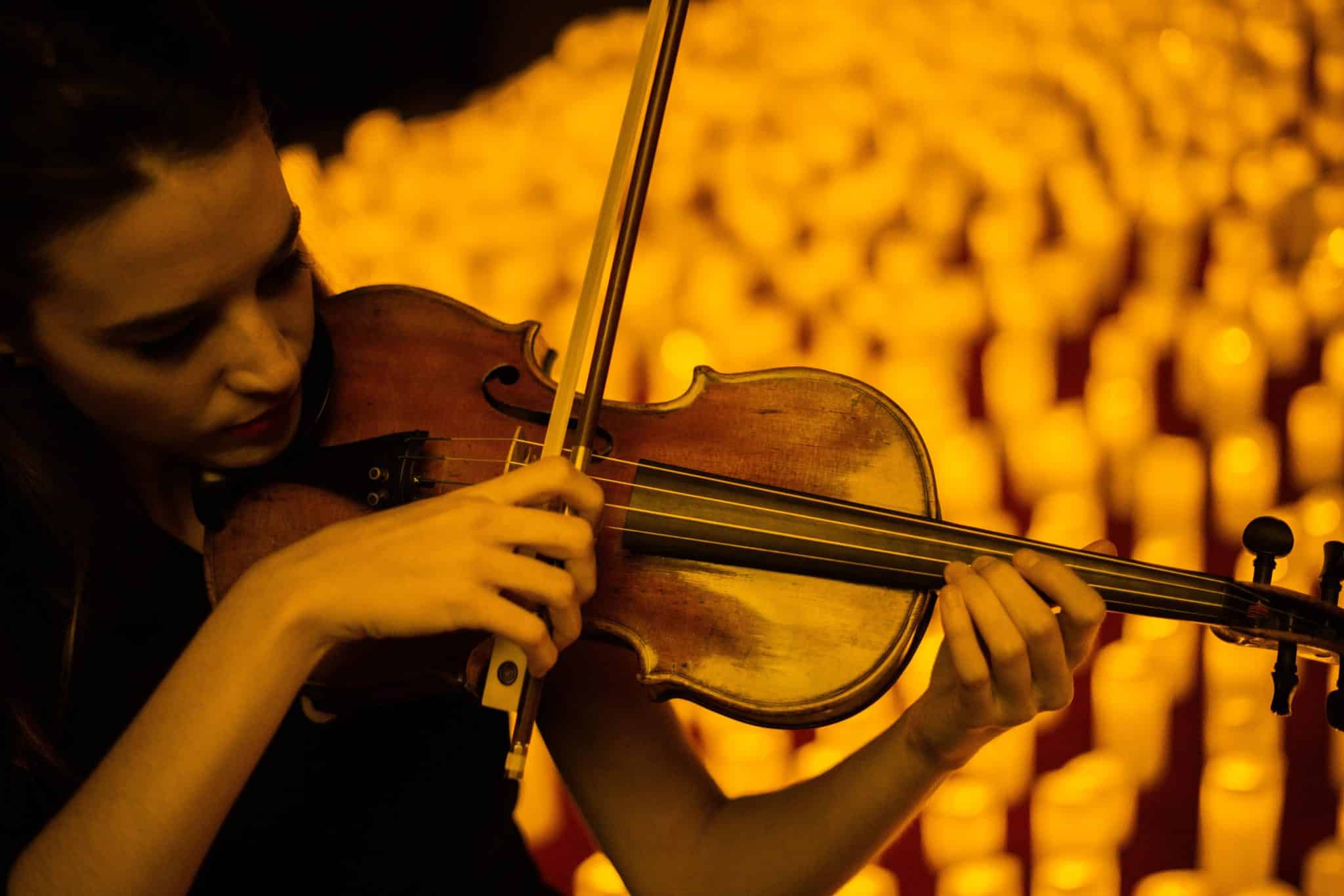 A woman plays a violin, surrounded by candles. 