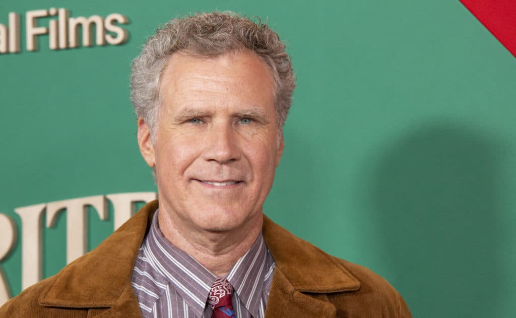 Actor Will Ferrell stands before a teal coloured background at a film premiere.