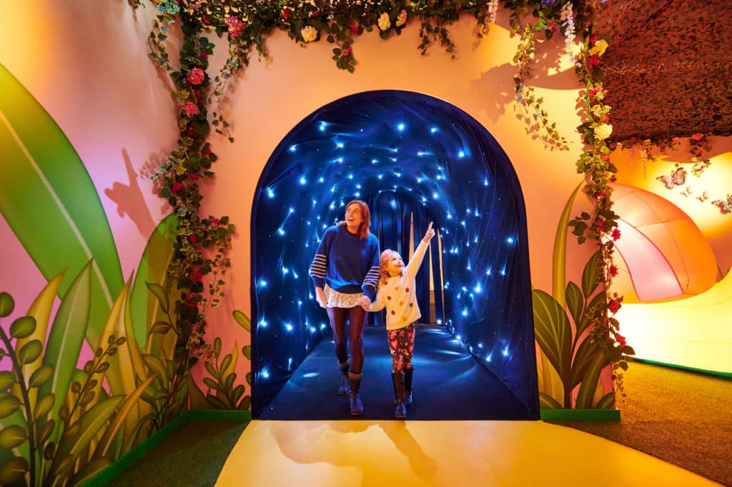a woman and child enter dreamland imaginarium through a sparkling walkway 
