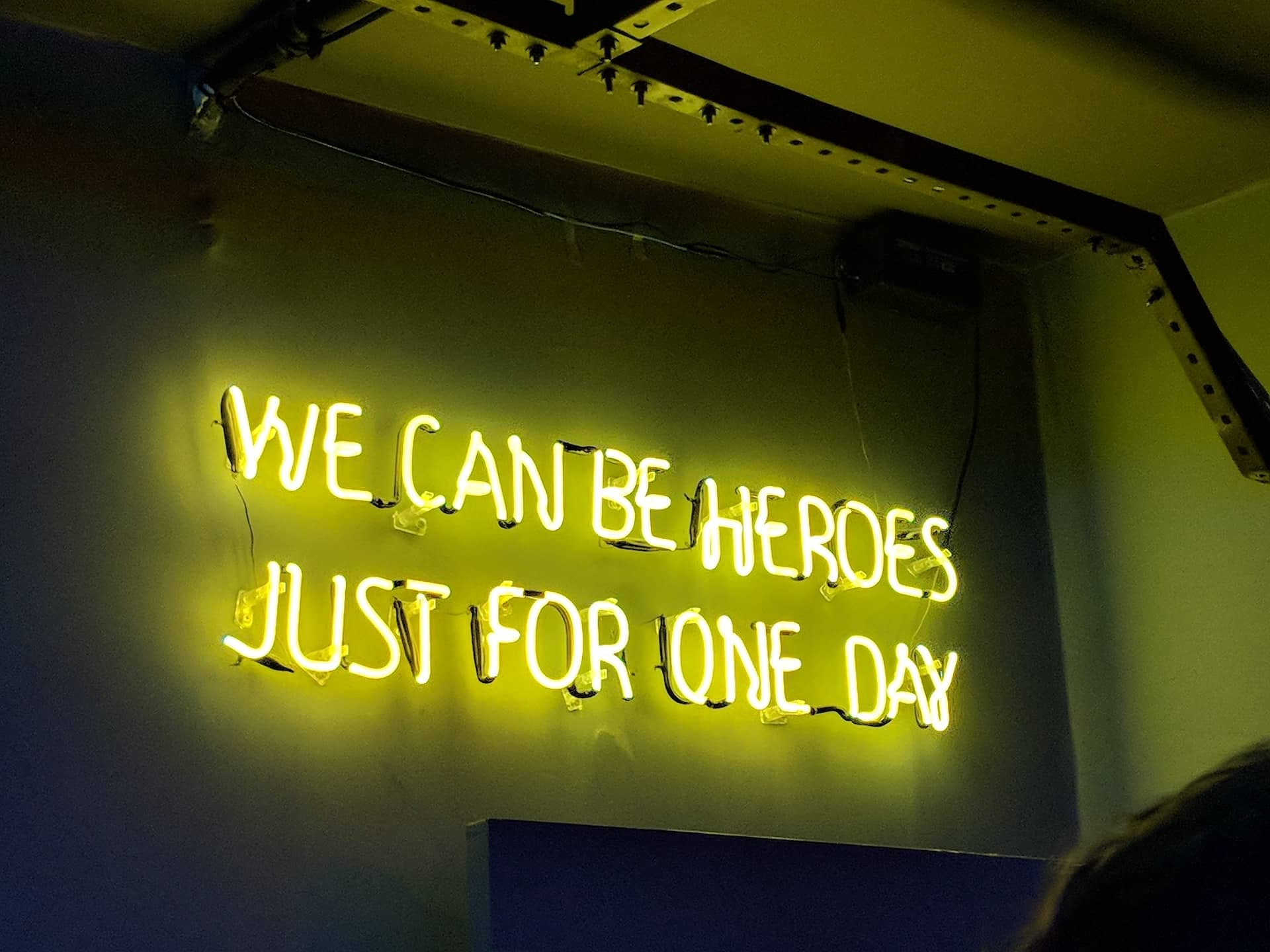A yellow, neon sign that reads ¨we can be heroes just for one day.¨