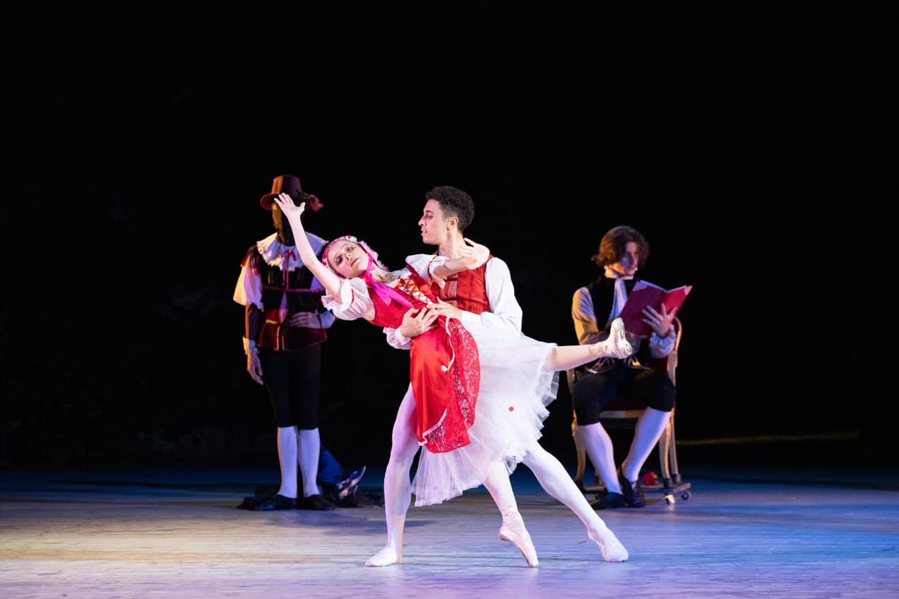Two ballet dancers dressed in red and white perform on a stage.