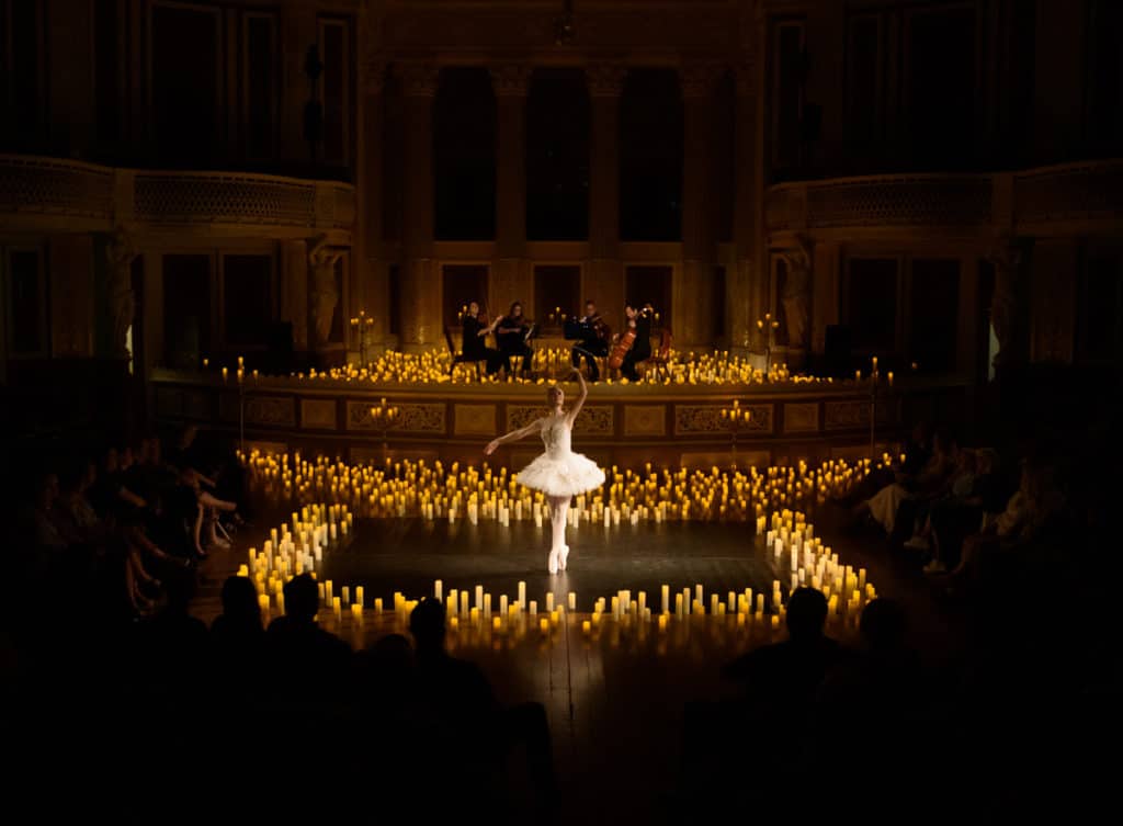 A single ballet dancer wearing white feathers surrounded by candles at St. George's Hall. 