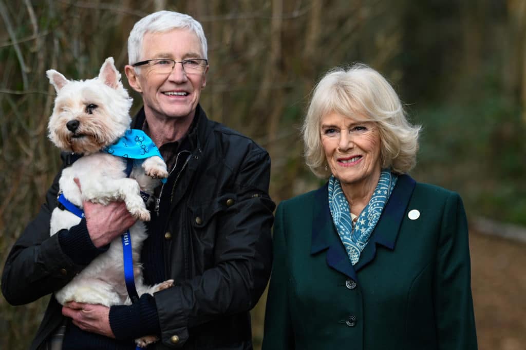 Paul O'Grady holds a Westie dog next to Camilla Parker Bowles, Queen consort.