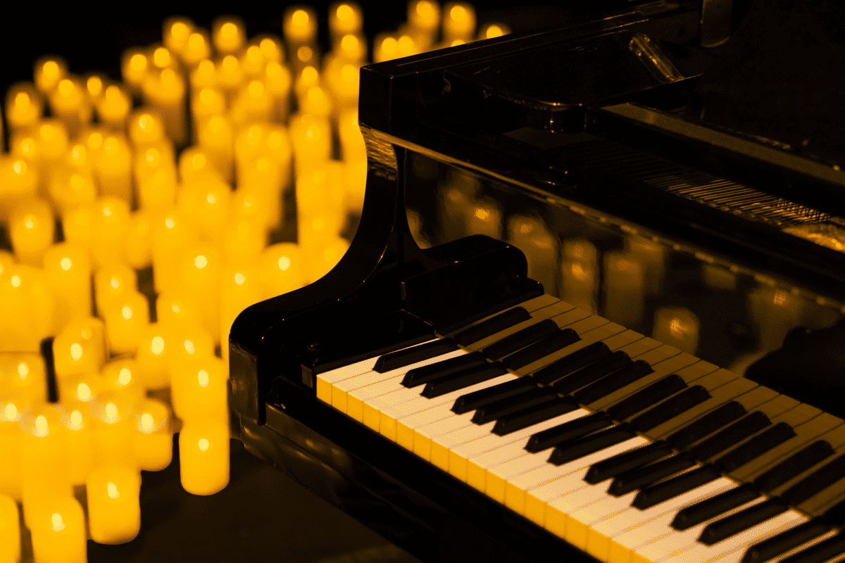 A close up of a piano keyboard with a sea of candles in the background.